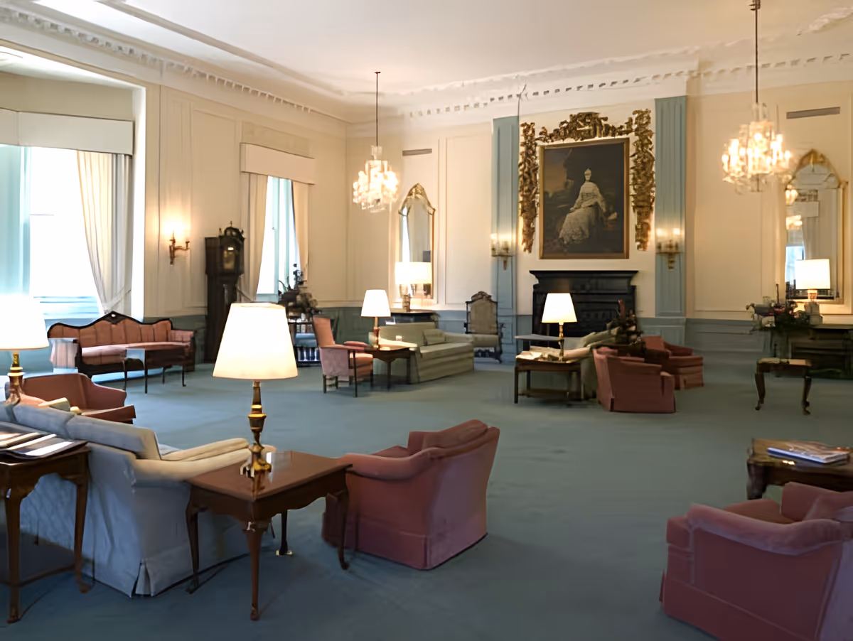 Large formal lounge with armchairs, sofas, table lamps, chandeliers, and a framed portrait above a fireplace.