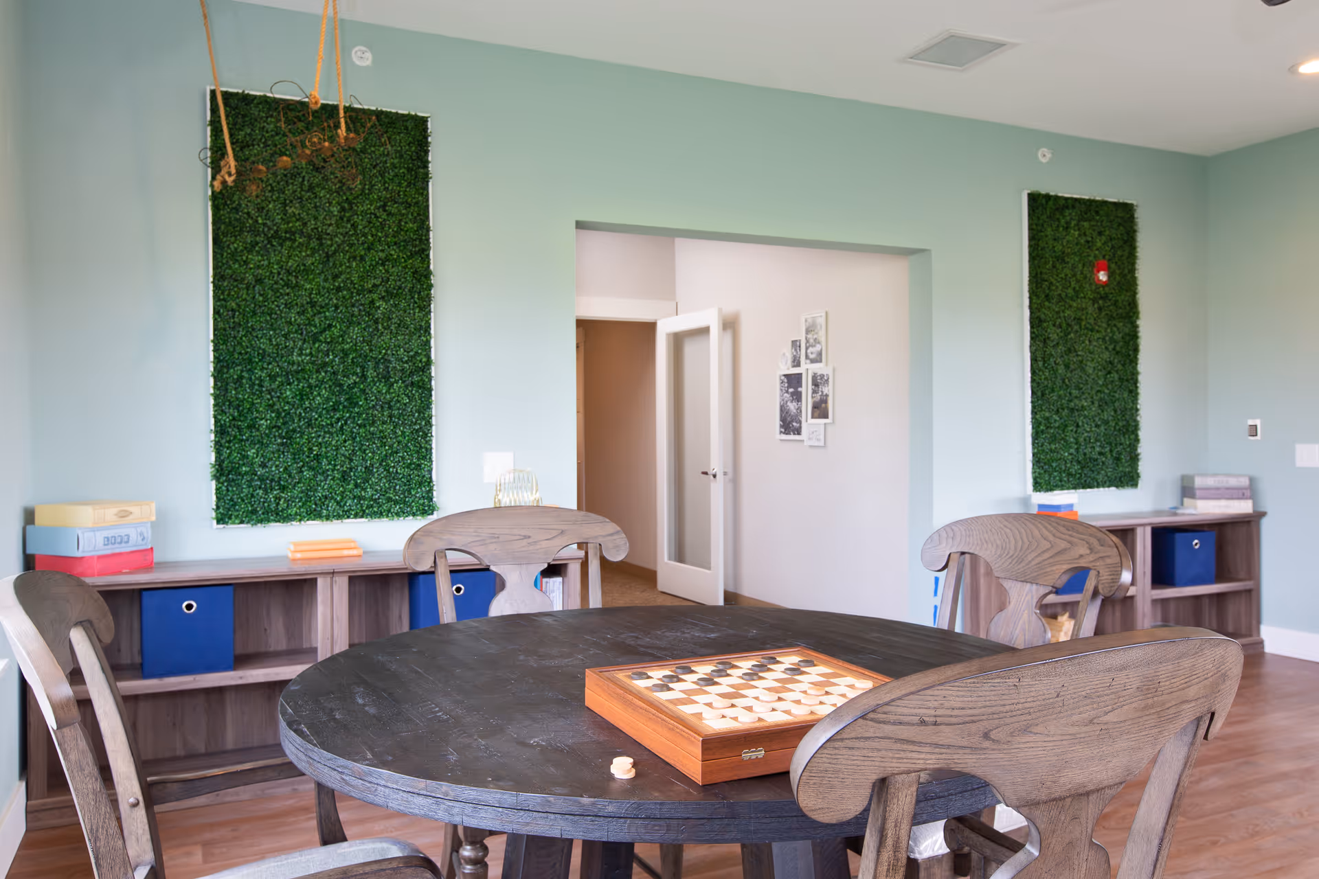 Round wooden table with chairs and chessboard in a light blue activity room.