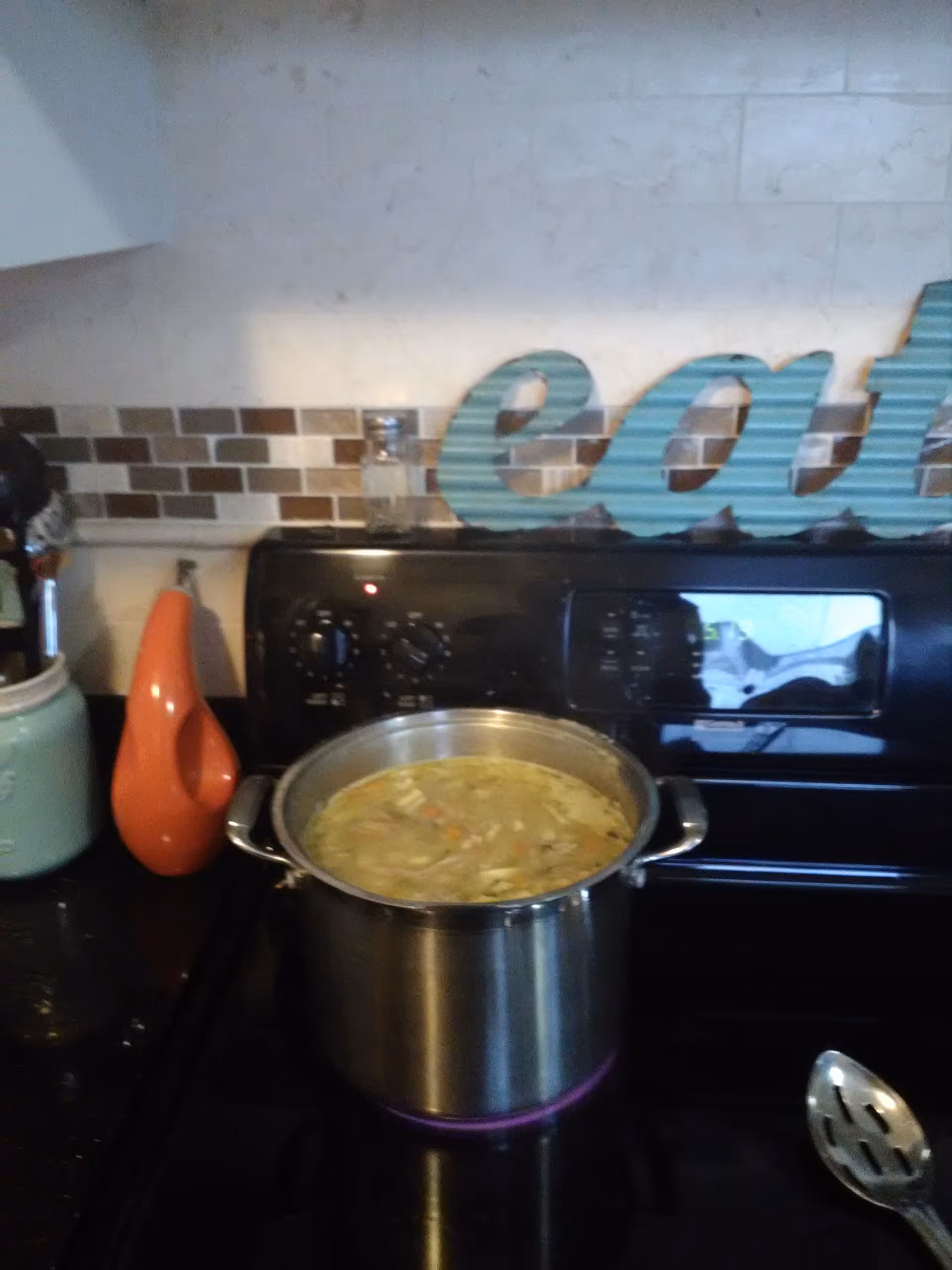 A pot simmers on a black stove in a bright kitchen with decorative letters.
