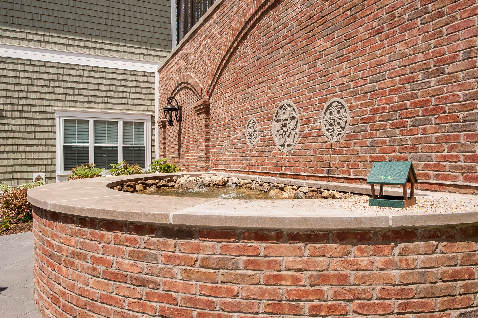 Curved brick water feature and decorative brick wall with three circular medallions outside a residential building.