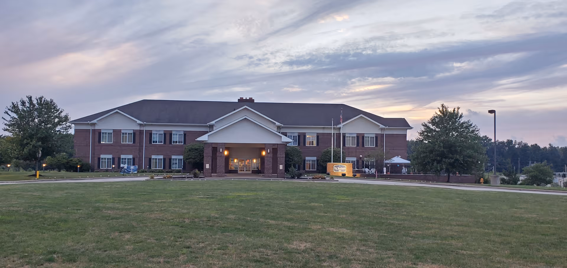 Brick senior living facility front with lawn and entrance at dusk.