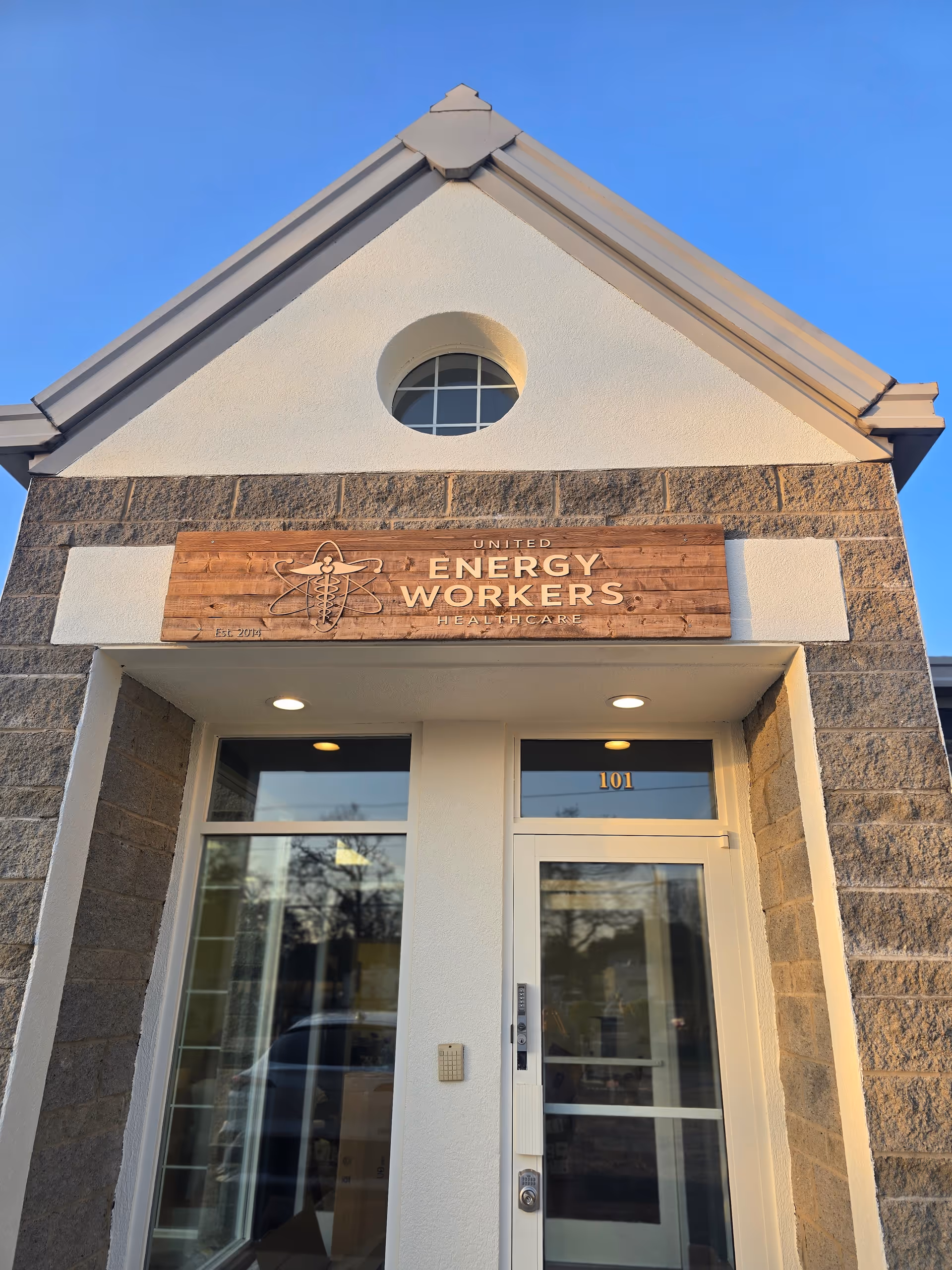 Front entrance of United Energy Workers Healthcare building with wooden sign.