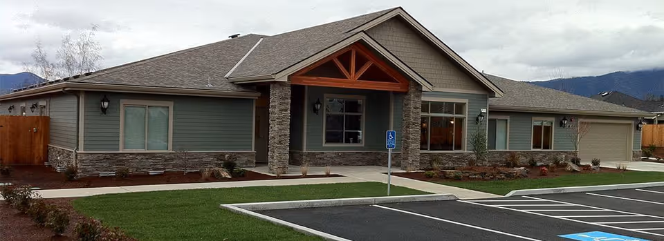 Single-story modern senior living facility with stone accents, green siding, front entrance, and parking.