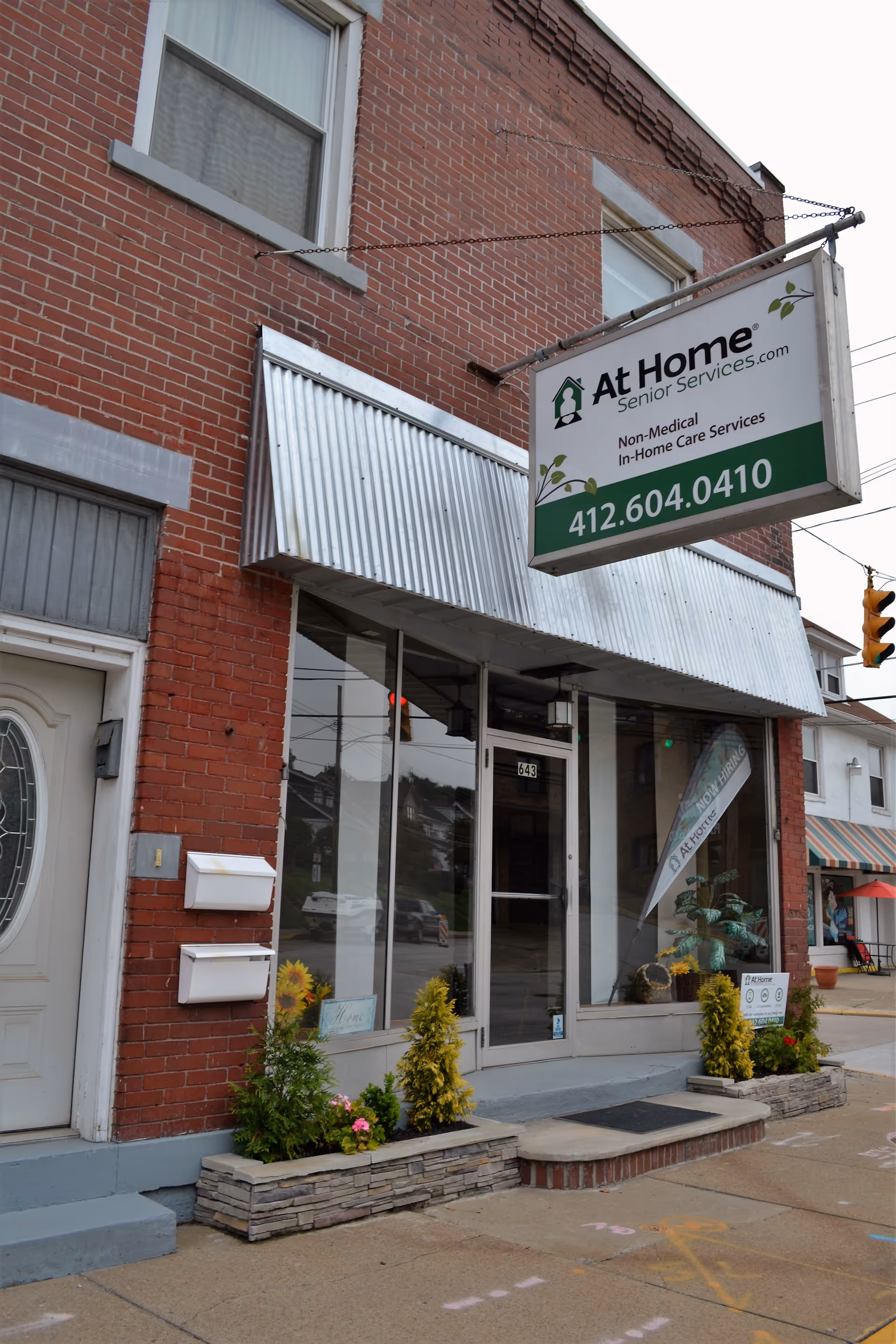 Brick storefront building with a hanging At Home Senior Services sign and entrance.