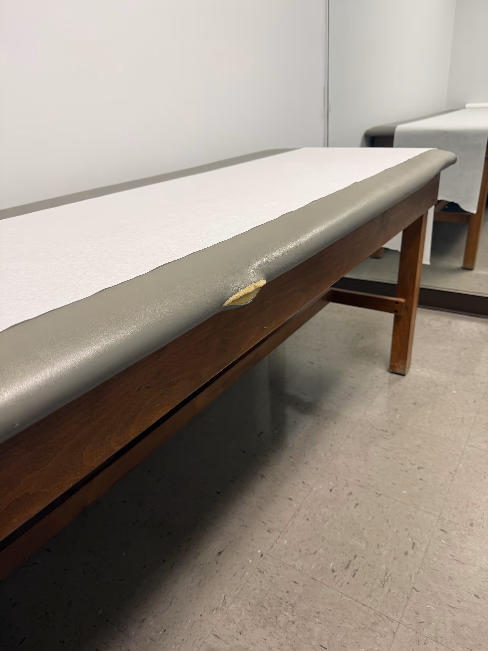 A padded examination table in a clinical room with a small upholstery tear.