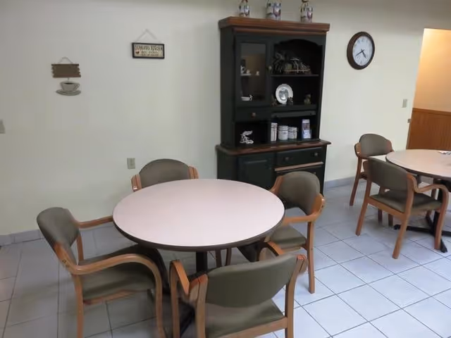 Round tables with chairs in a dining room, cabinet and wall clock in background.