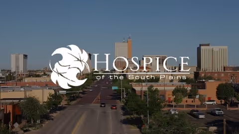 Outdoor city street scene with tall buildings and trees, featuring HOSPICE of the South Plains watermark.
