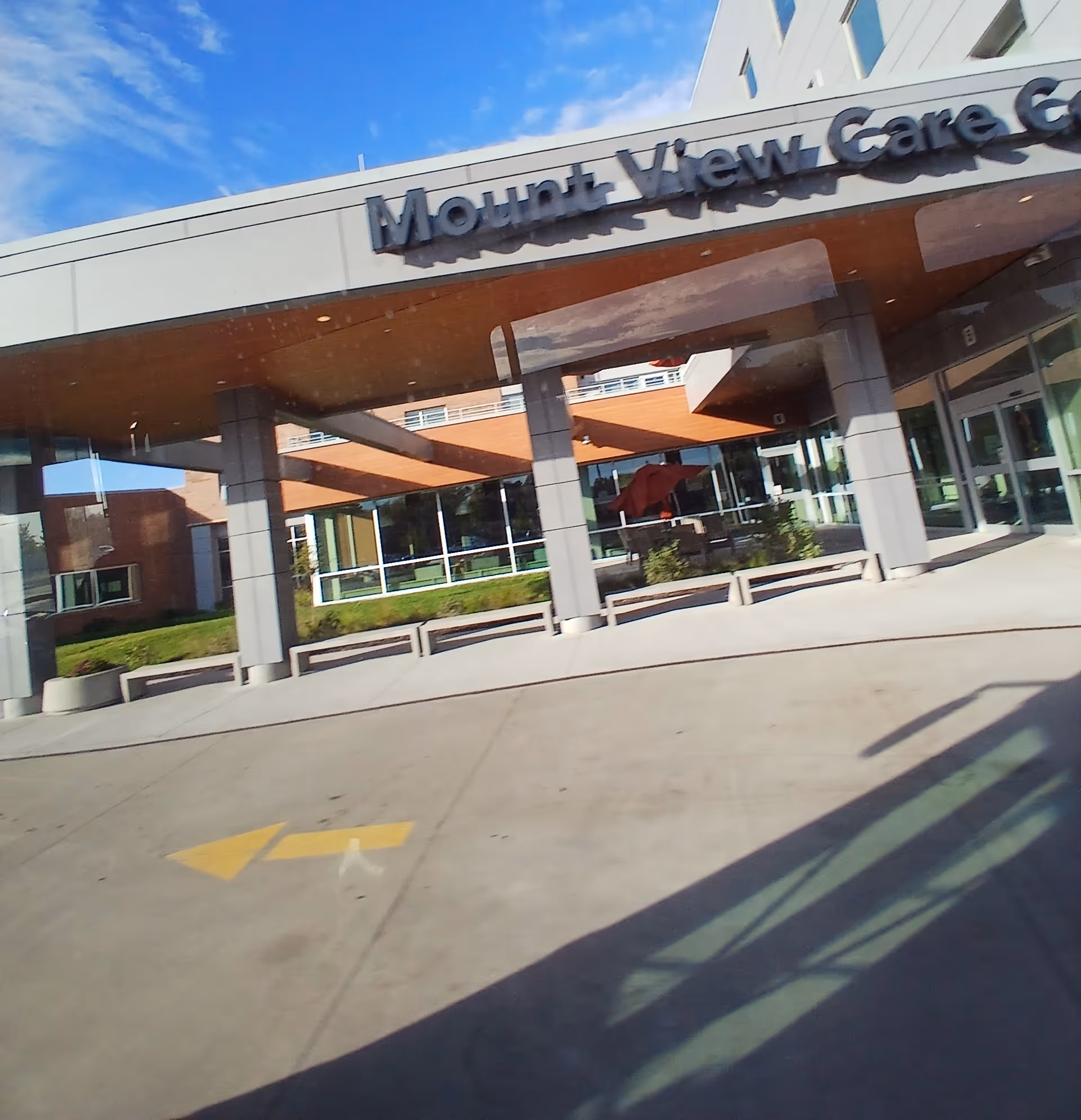 Exterior view of a senior living facility entrance with glass walls and a covered patio.