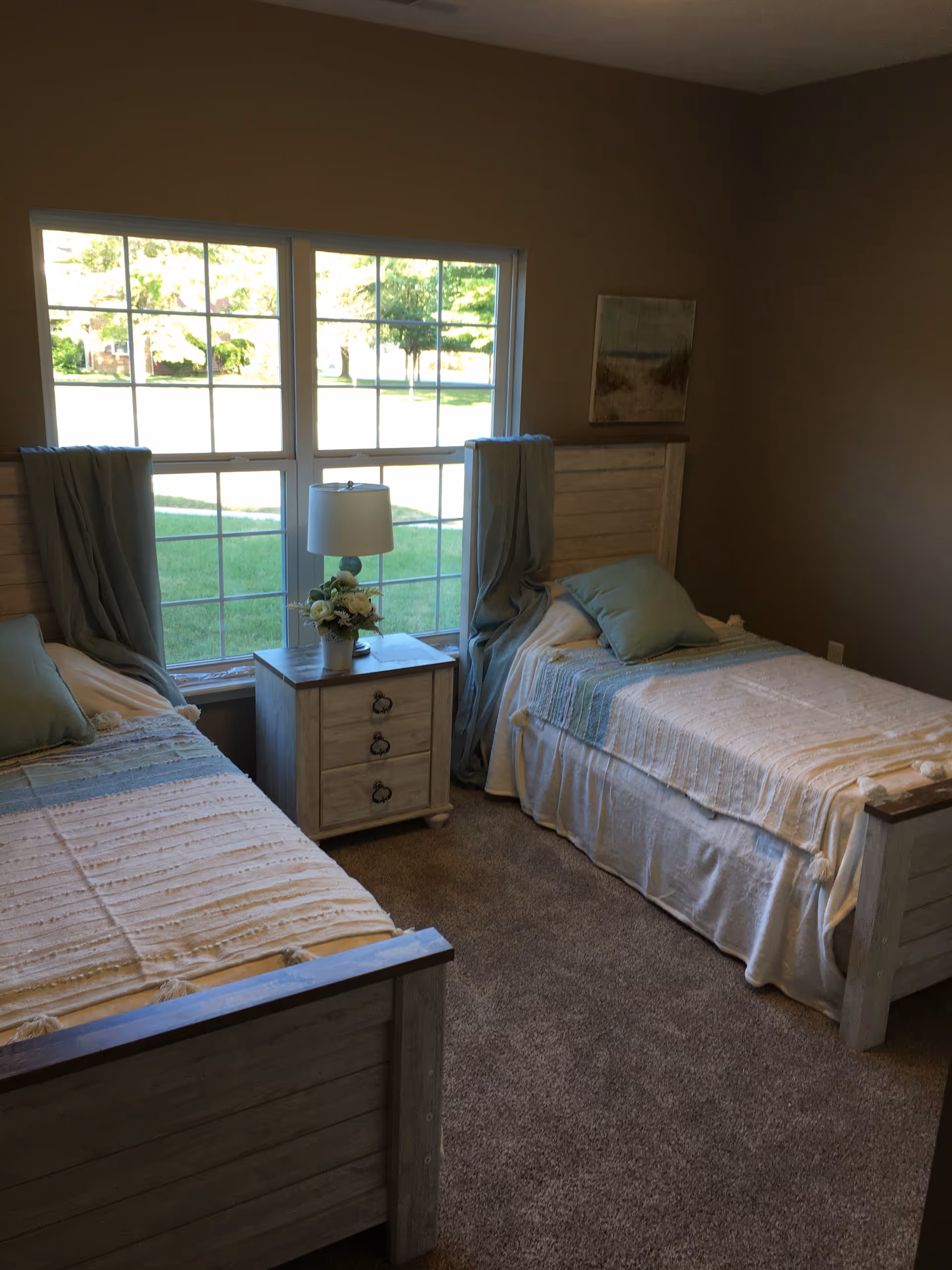 Two twin beds separated by a nightstand with lamp in a bright bedroom.