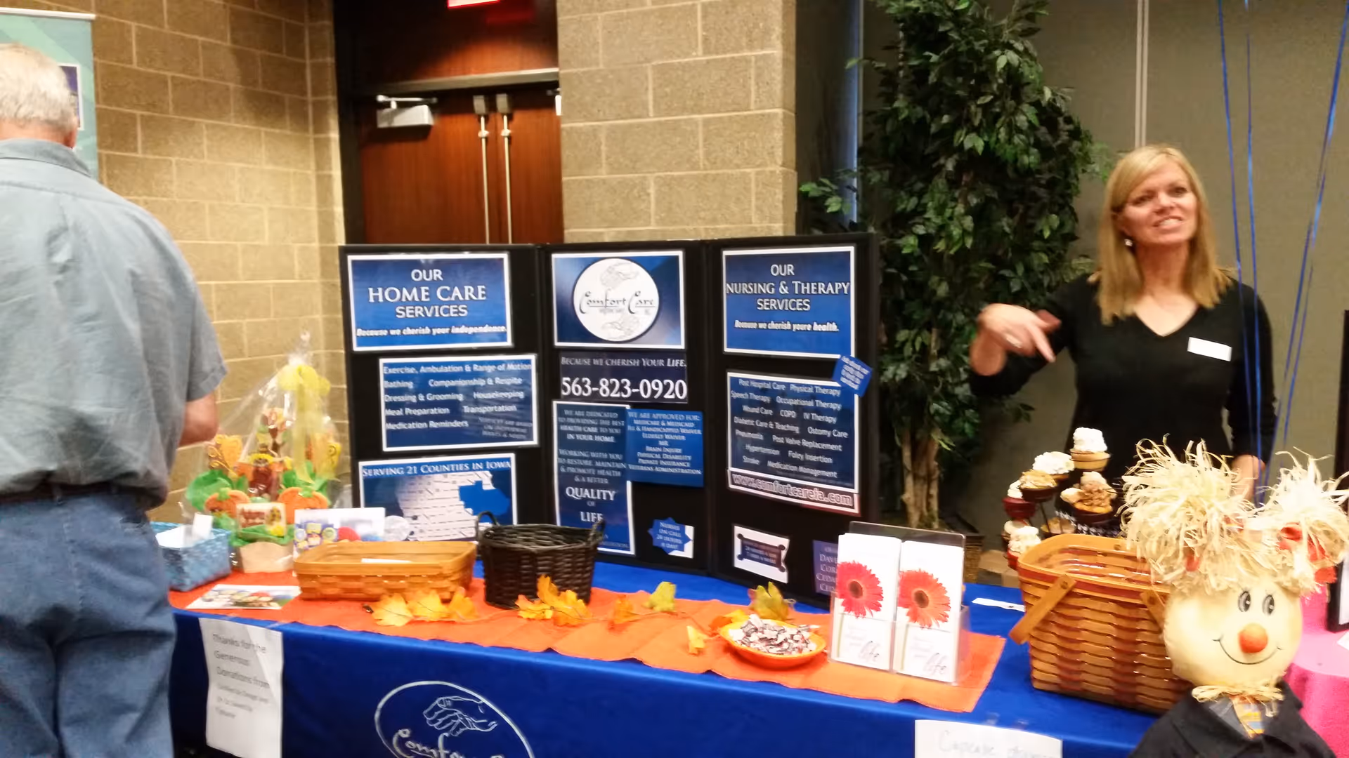 Two adults stand by a vendor table with informational boards inside a facility hallway.