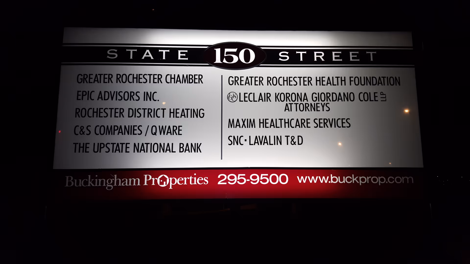 Nighttime exterior signboard listing multiple company names near State Street 150.