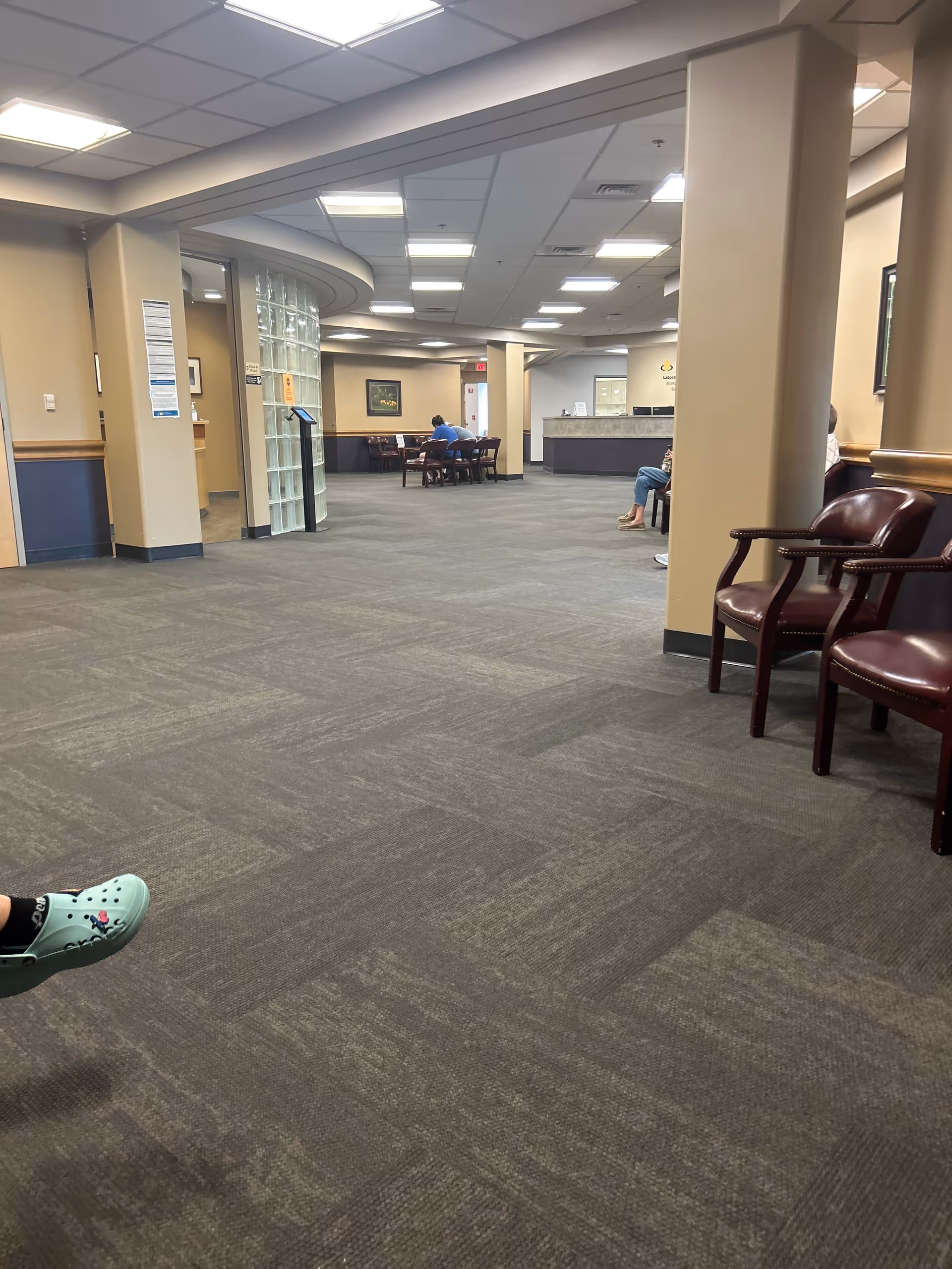 Hospital lobby with seating area, curved reception desk, pillars, and several people seated.