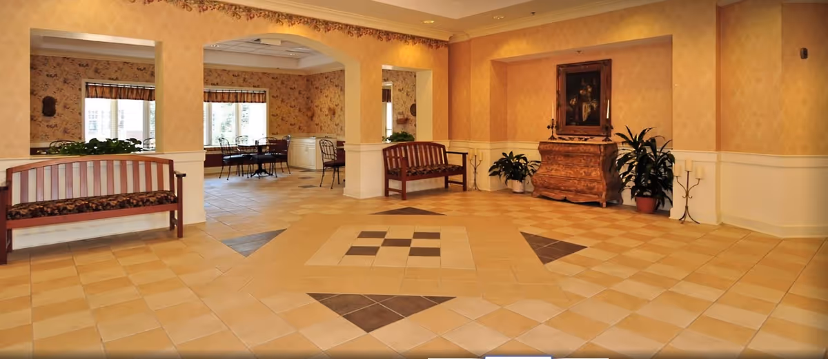 Spacious tiled common area with wooden benches, decorative chest and plants, and a dining area visible through arched openings.