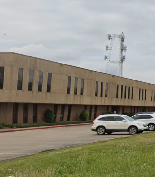 Exterior view of a beige senior care building with windows and parked cars.