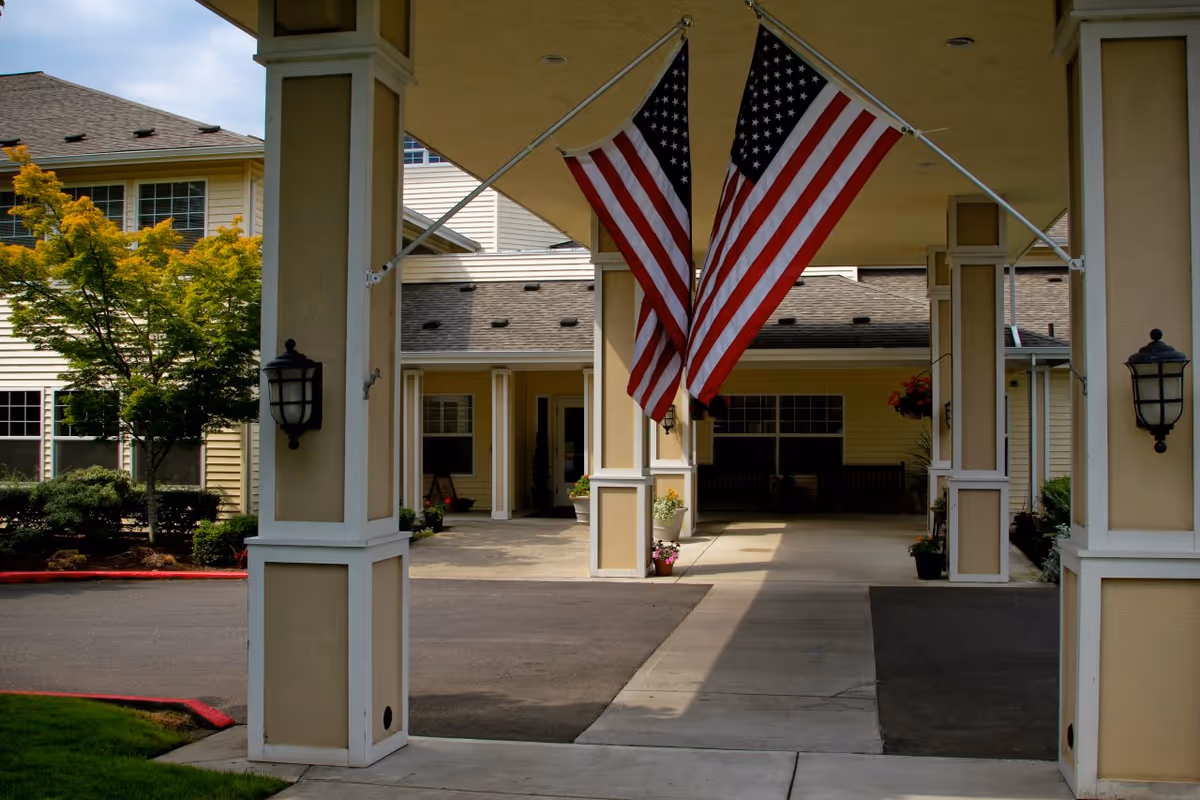 Entrance of Prestige Senior Living Huntington Terrace with two American flags under a covered drop-off.