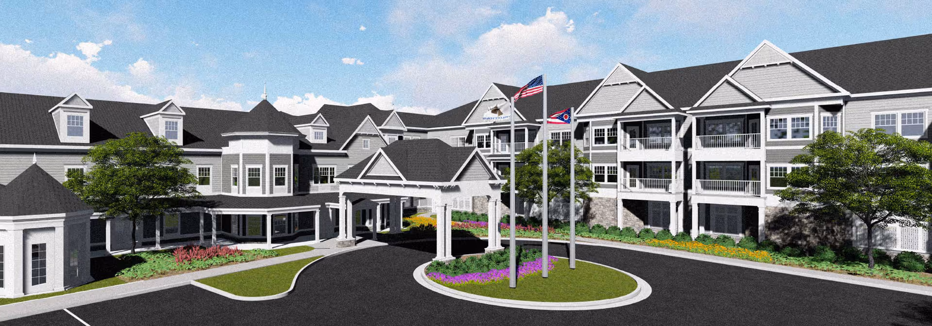 Front exterior of Traditions at Camargo senior living building with a porte-cochère, flagpoles, balconies, and a landscaped circular driveway.