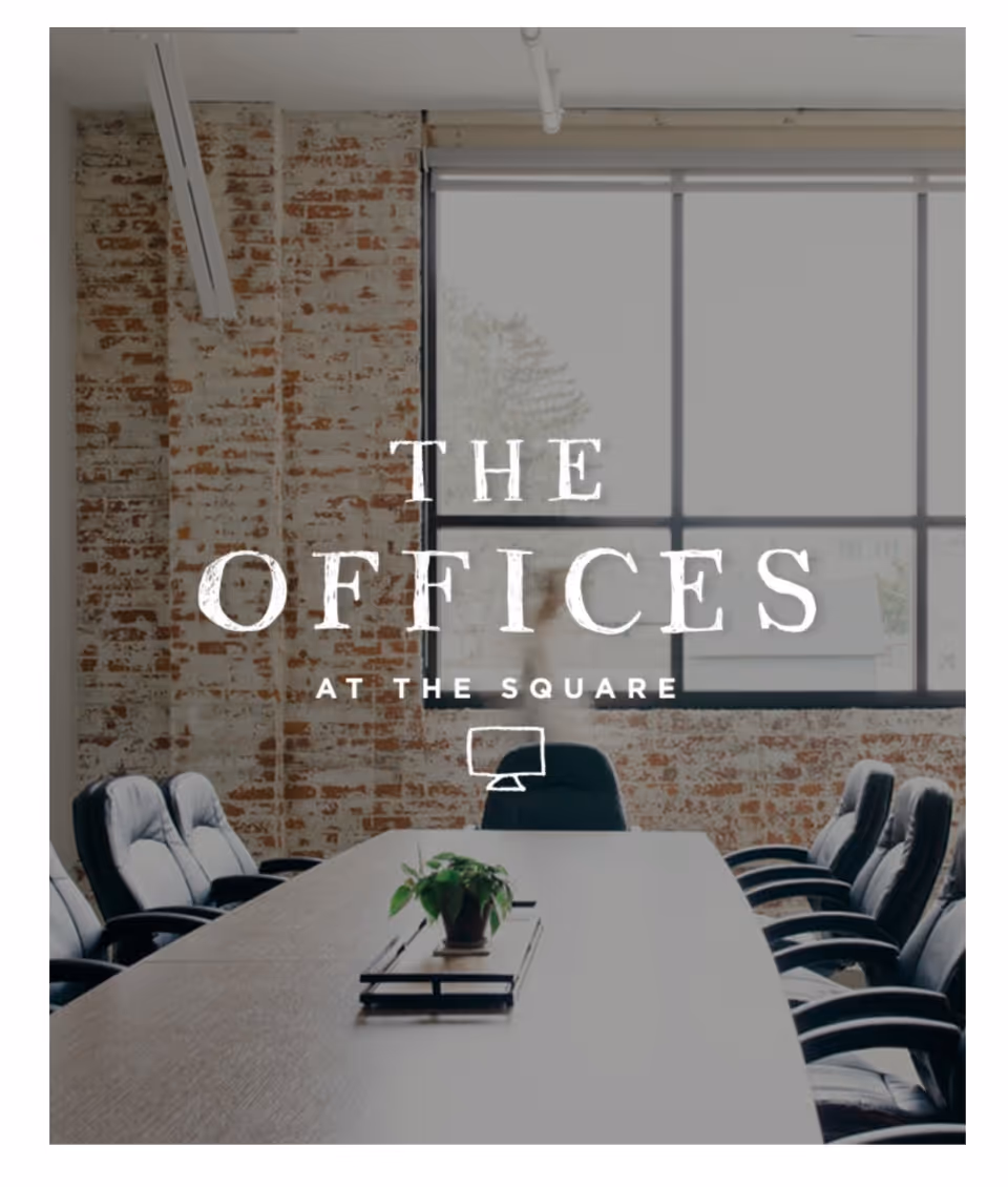 A long conference table with black chairs beside a brick wall and large window.