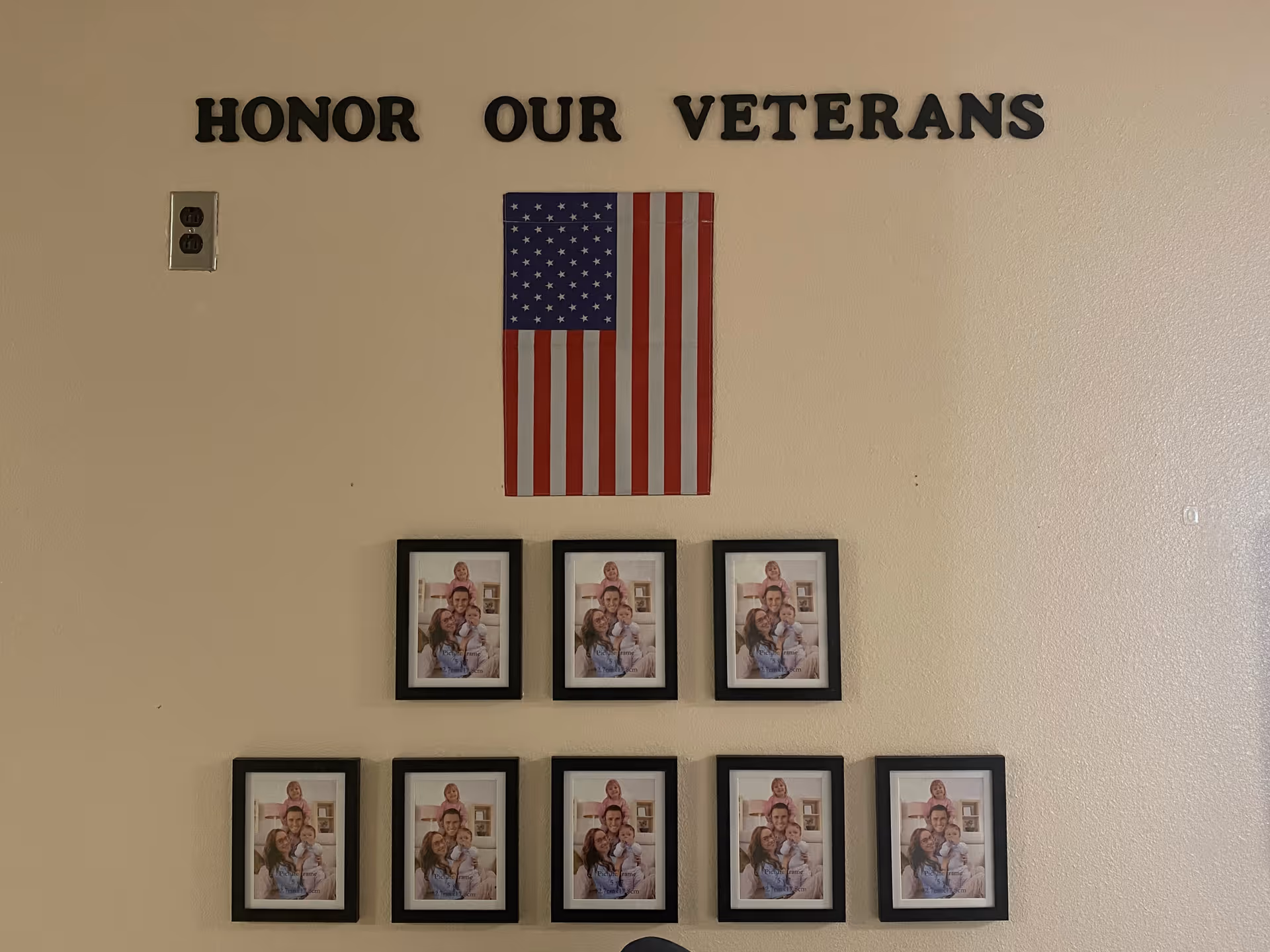 Interior wall display reading 'HONOR OUR VETERANS' with an American flag above a grid of framed family photos.