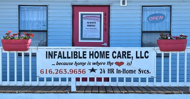 Blue building exterior featuring a white banner for Infallible Home Care, pink door, and window planters.