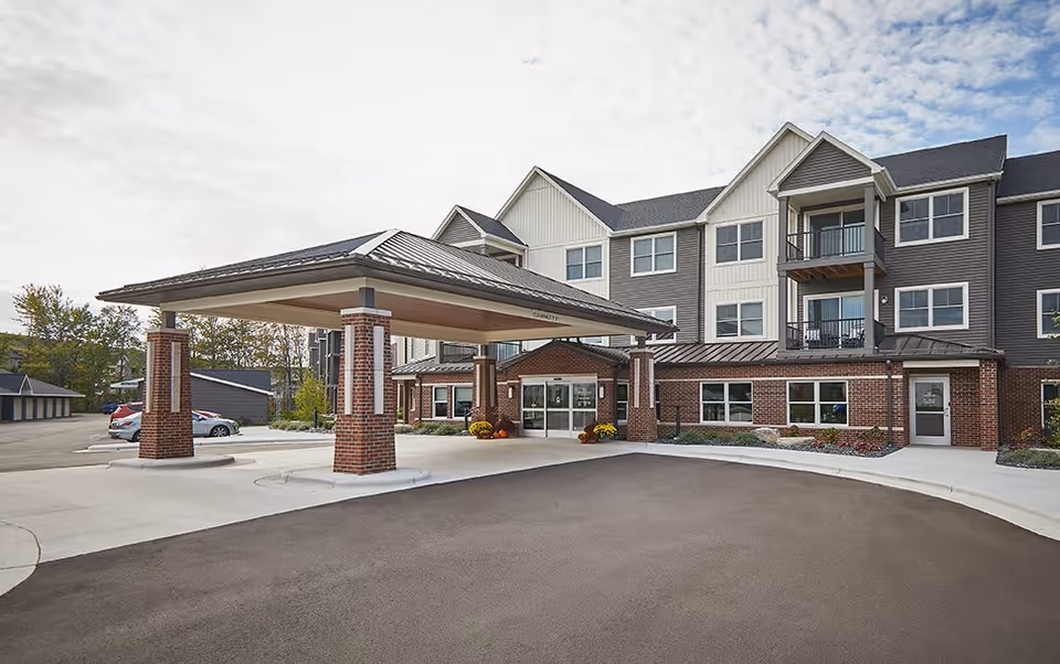 Front entrance of a multi-story senior living building with a covered porte-cochère and parking area.