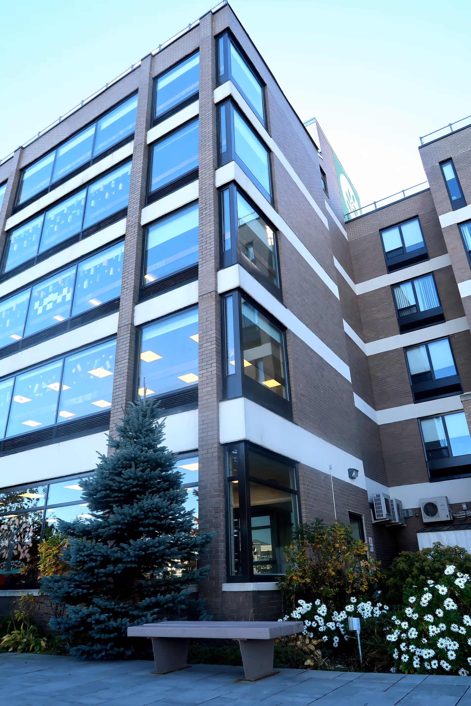 Modern brick nursing facility exterior with large glass windows and a small outdoor bench.