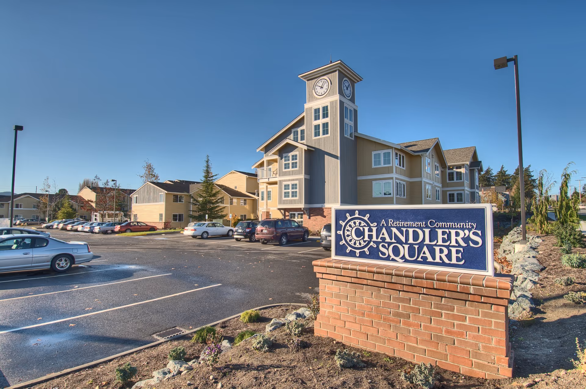 Exterior view of Chandler's Square Retirement Community with a clock-tower building and parking lot.