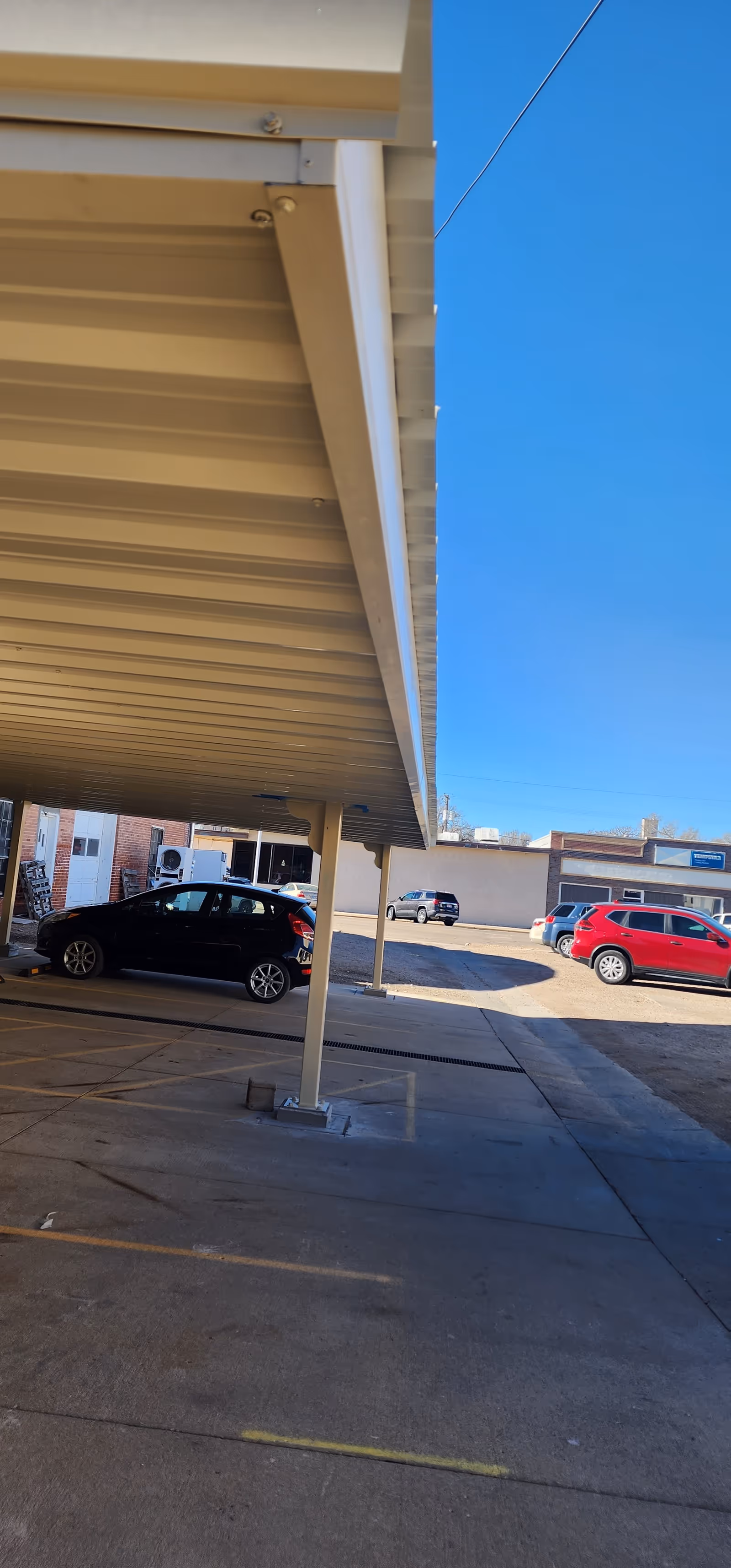 Covered outdoor parking area with cars, support columns, and blue sky.