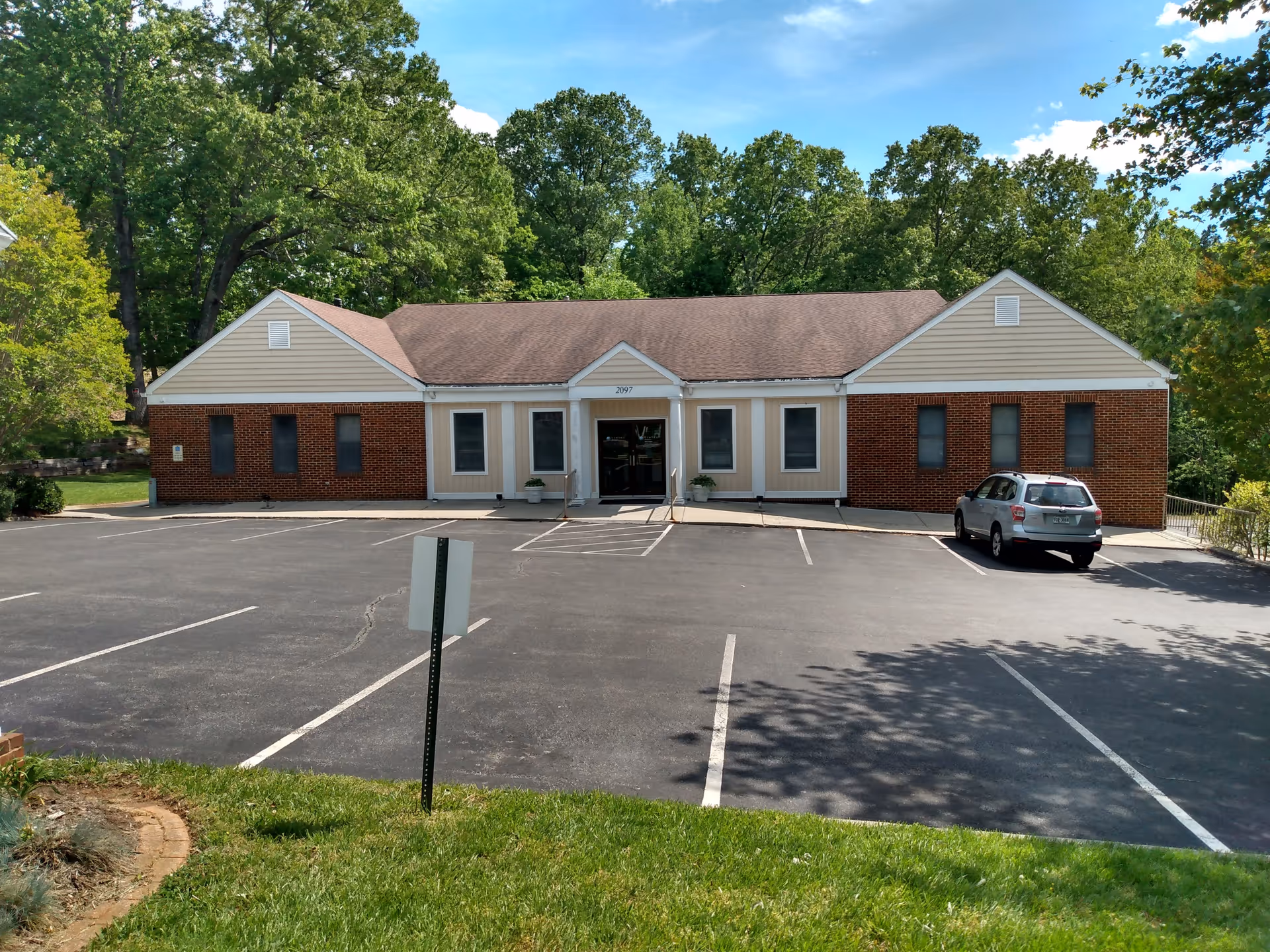 Front view of a single-story brick building with a parking lot and trees.