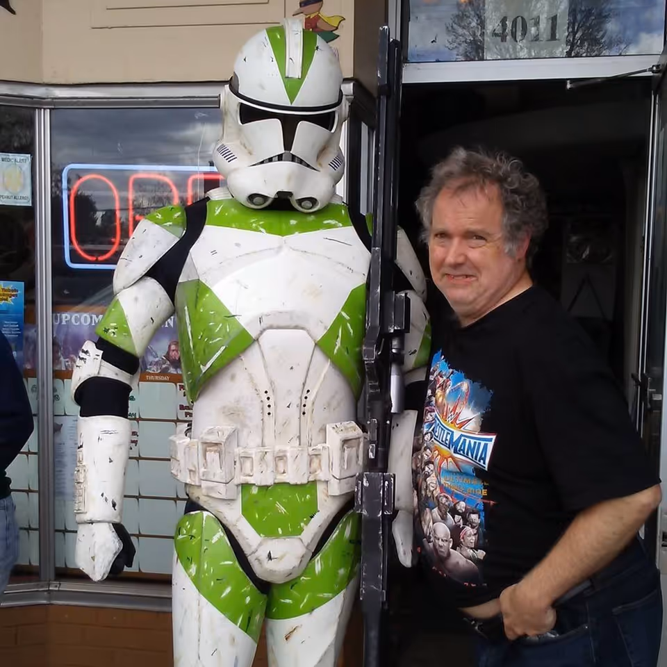 Man stands beside a life-size green and white armored figure outside a storefront.