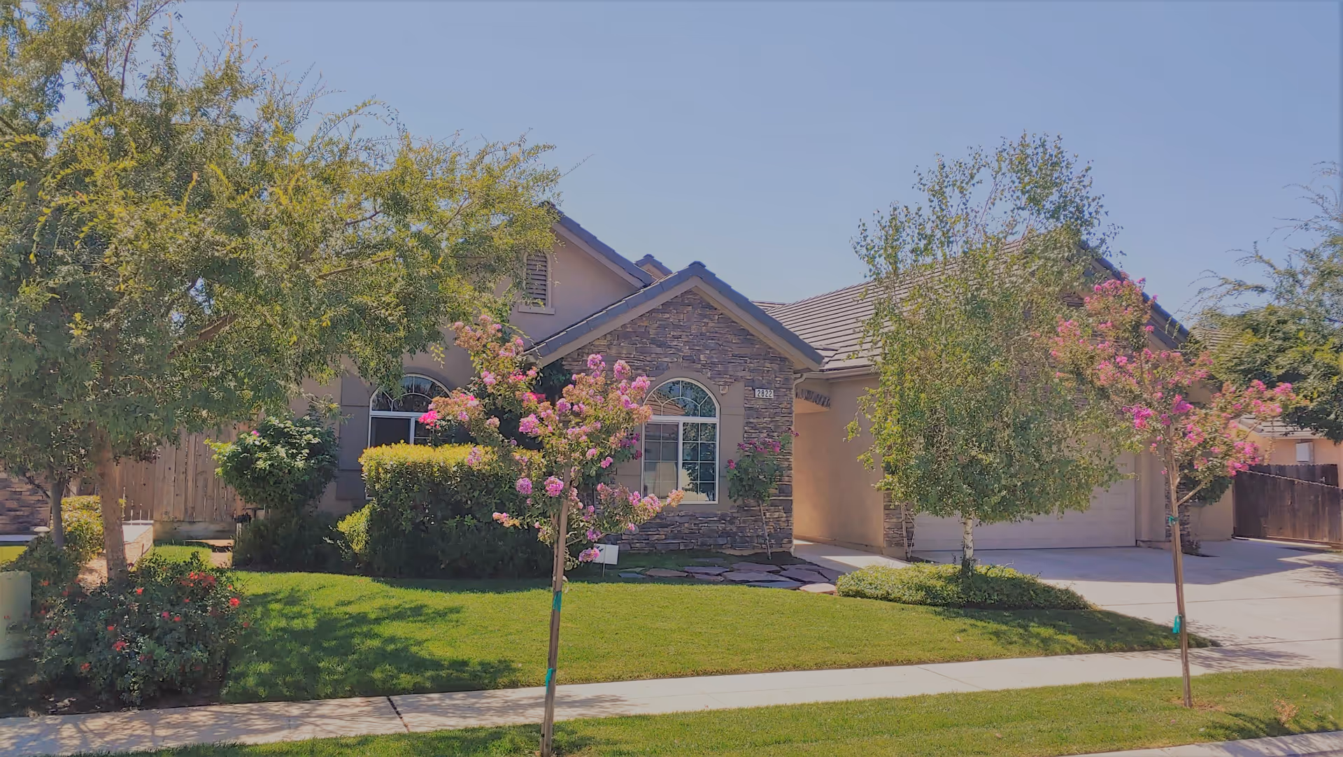 Front view of a single-story residential care home with trees and a driveway.
