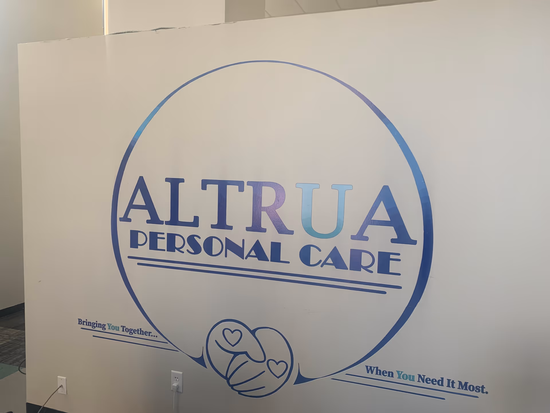 A large circular Altrua Personal Care logo sign on an interior wall.
