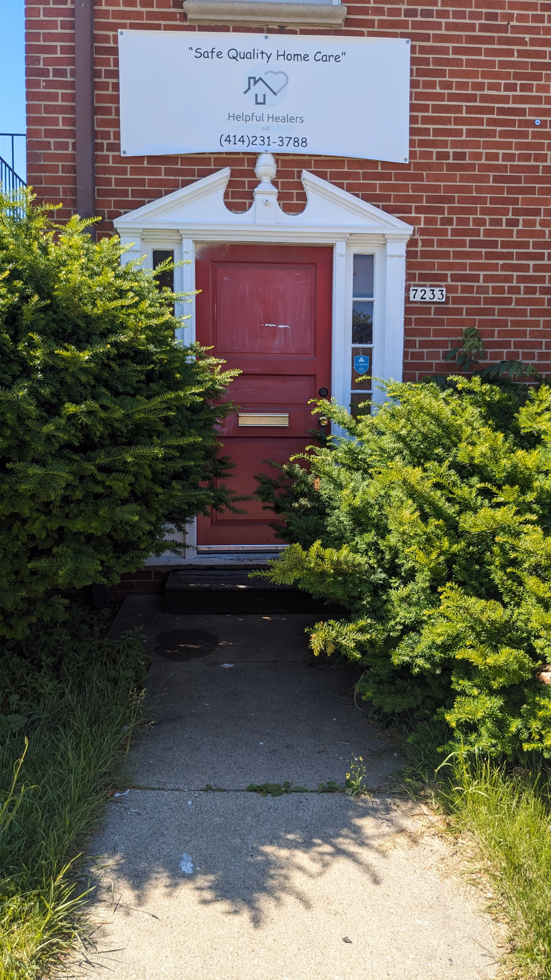 Brick building entrance with a red door, shrubs, and Helpful Healers sign above.