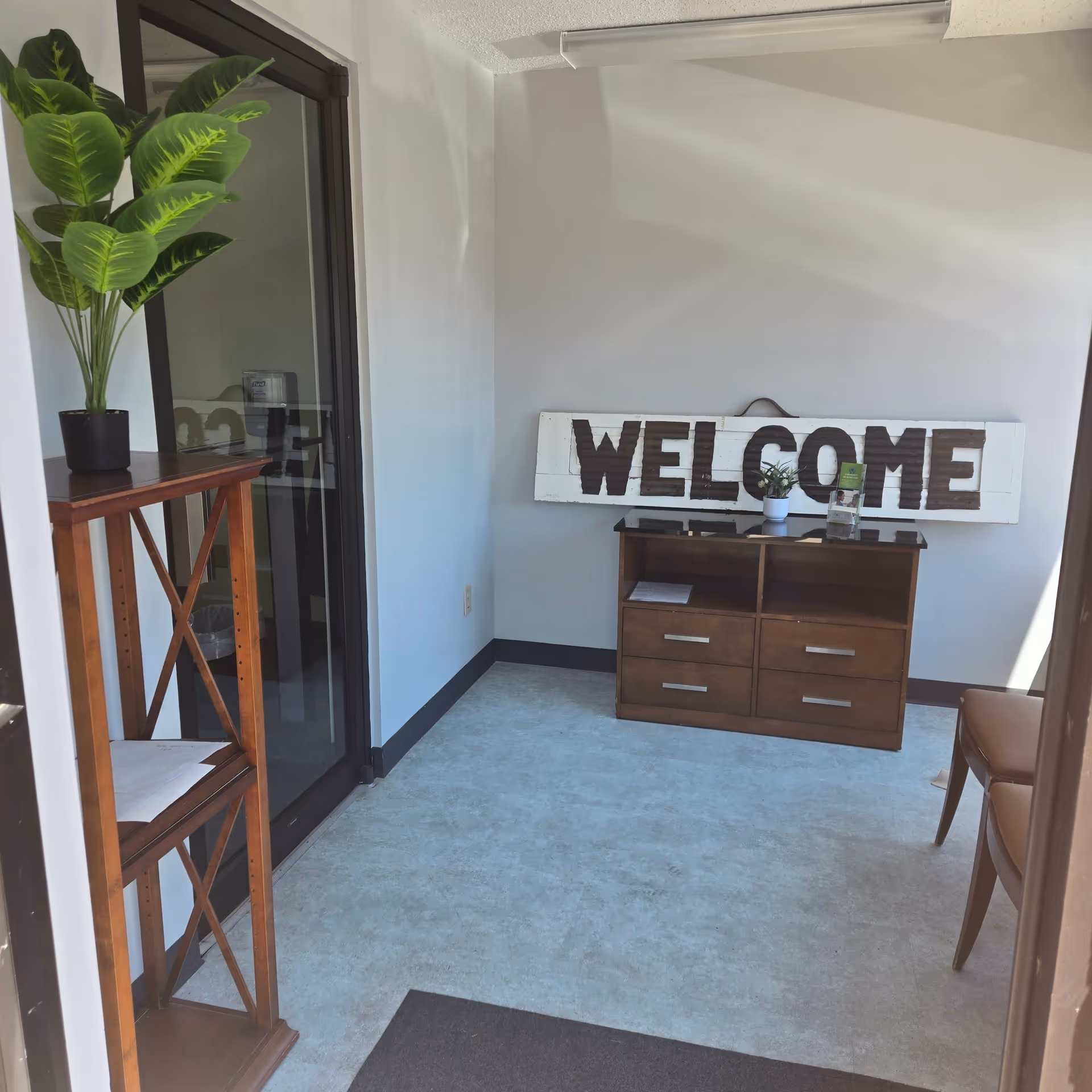 Entrance foyer with a welcome sign, wooden dresser, plant, and glass doors to outside.