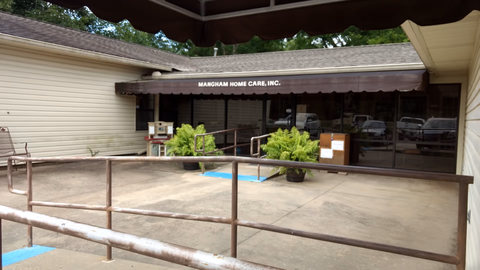 Exterior view of Mangham Home Care entrance with awning, ramp, and potted plants.