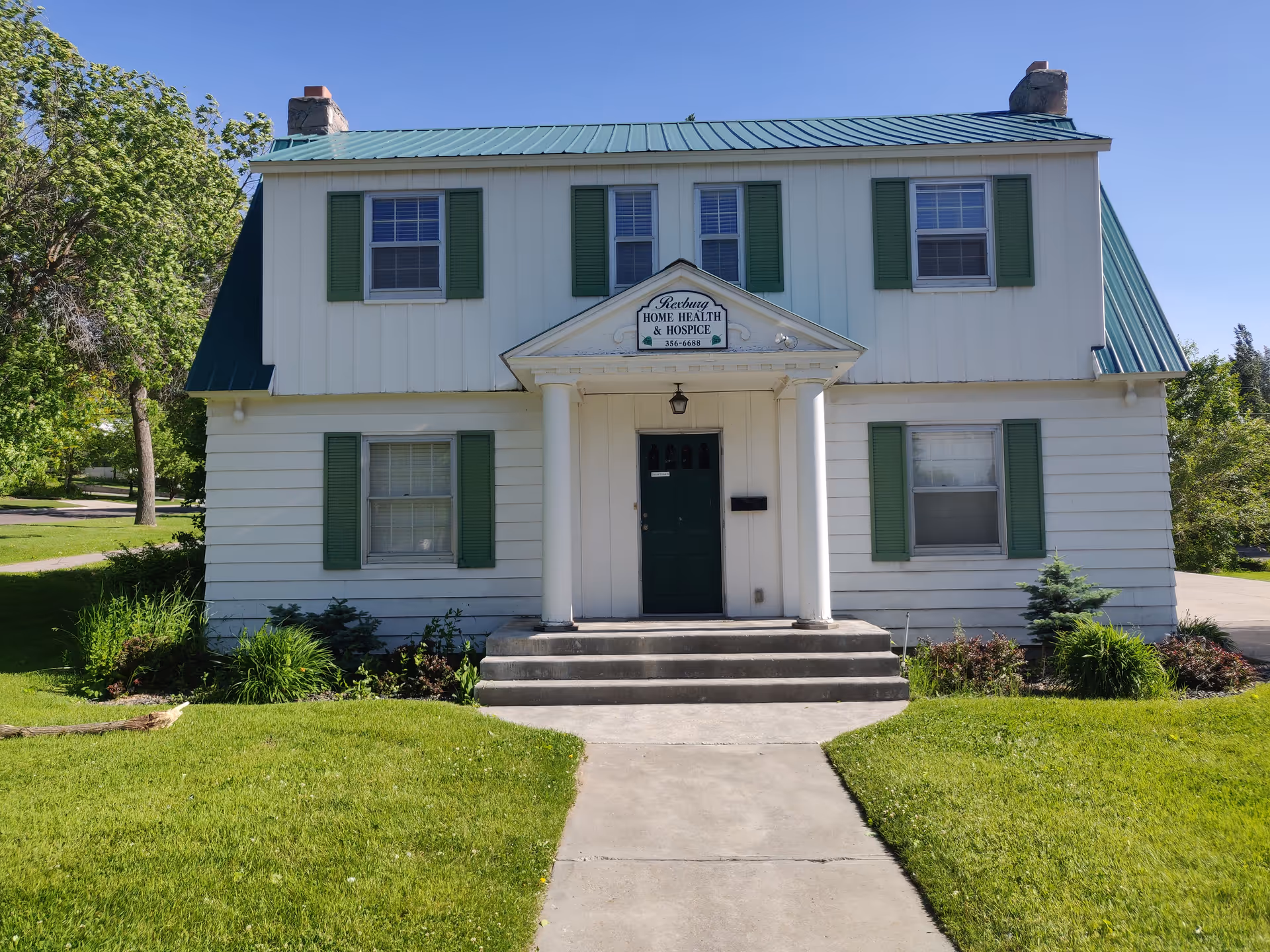 White two-story building with green shutters and a sign reading Rexburg Home Health & Hospice.