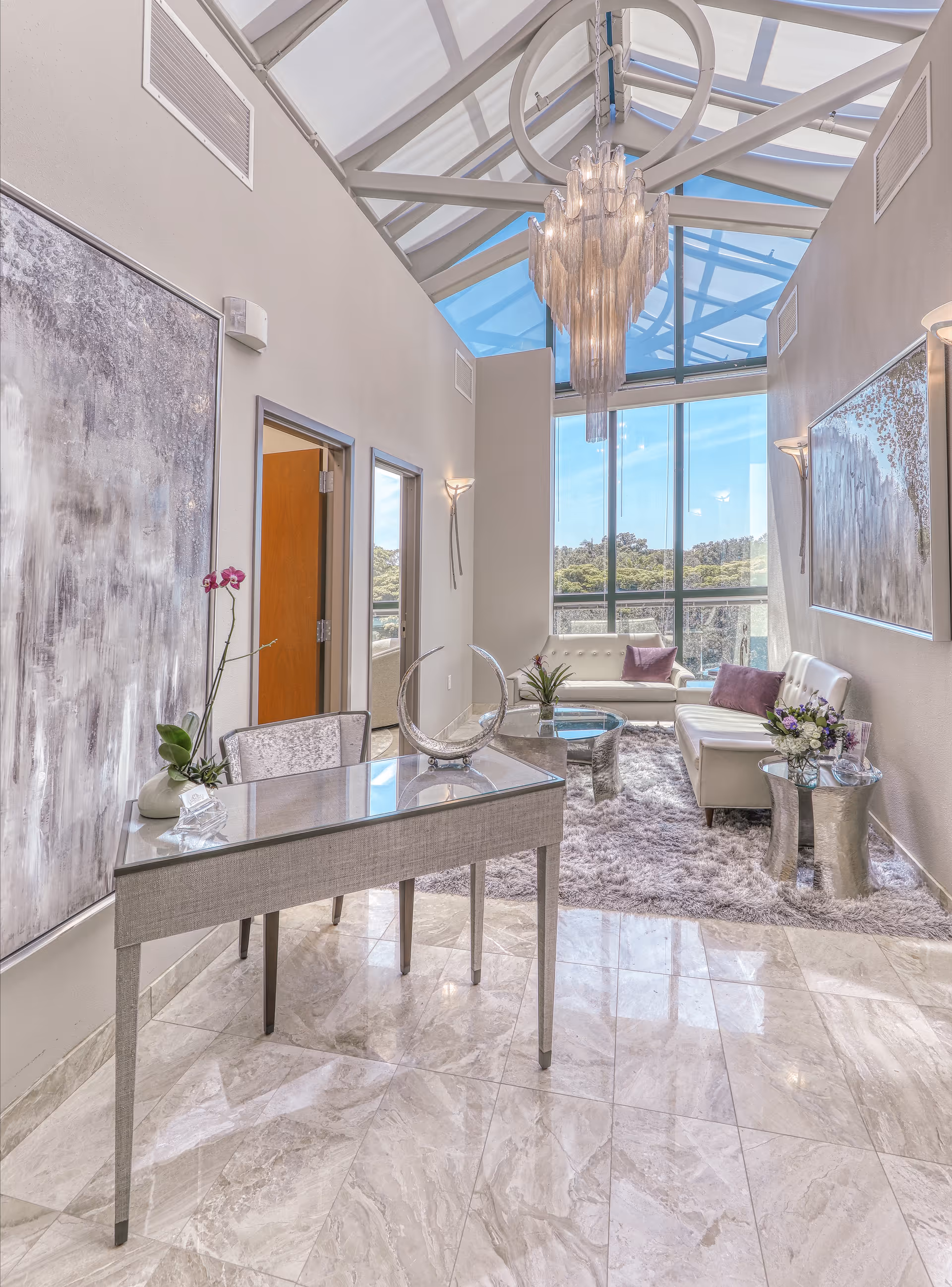Bright modern lobby with glass skylight, chandelier, and seating area.
