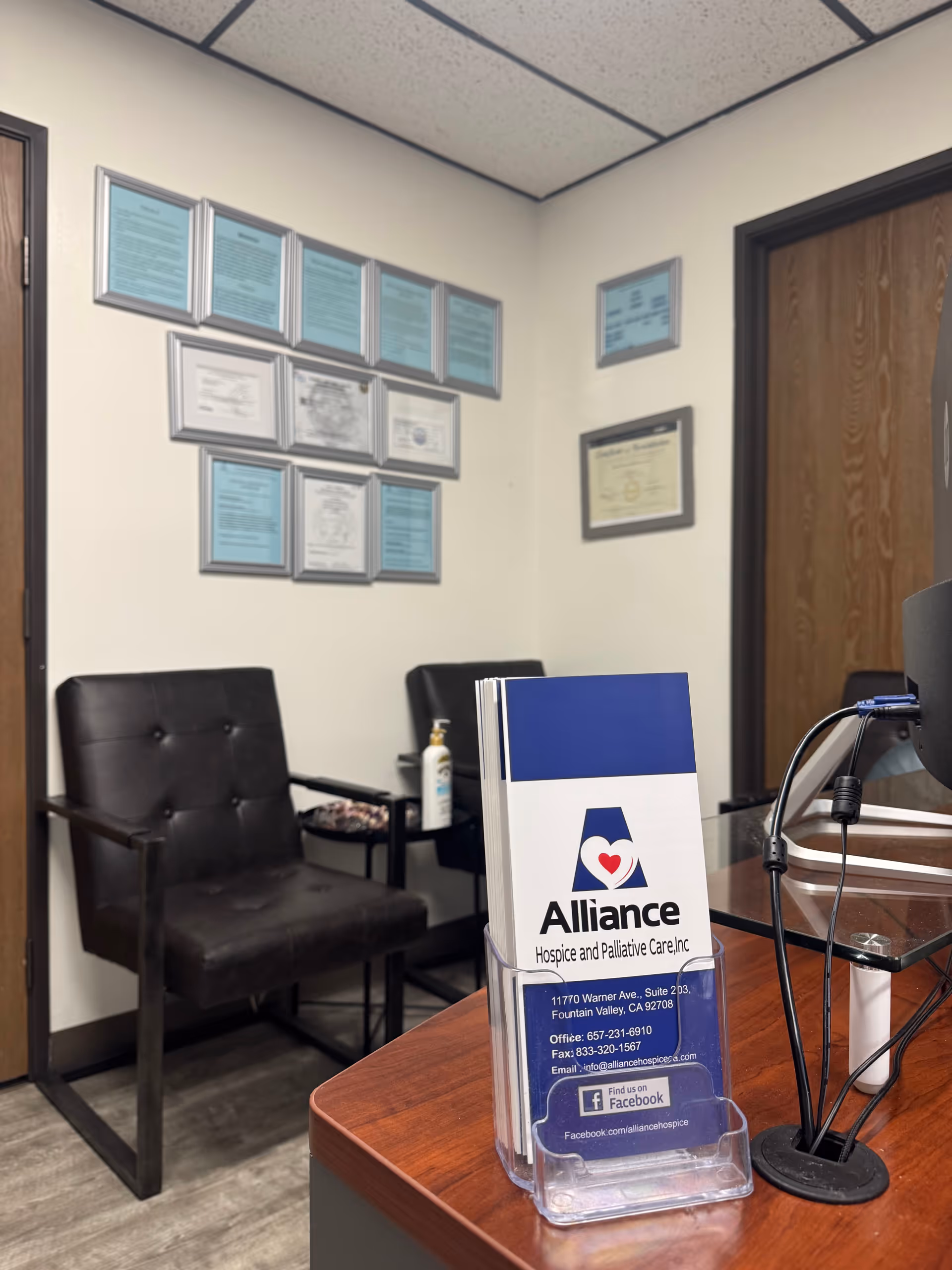 Office reception area with brochure stand, chairs, certificates on walls, and doorway.