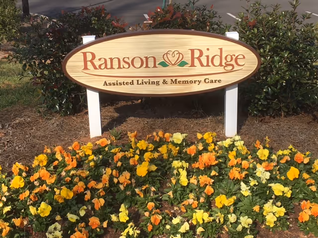 Outdoor sign reading 'Ranson Ridge' with colorful flowers in front of the facility