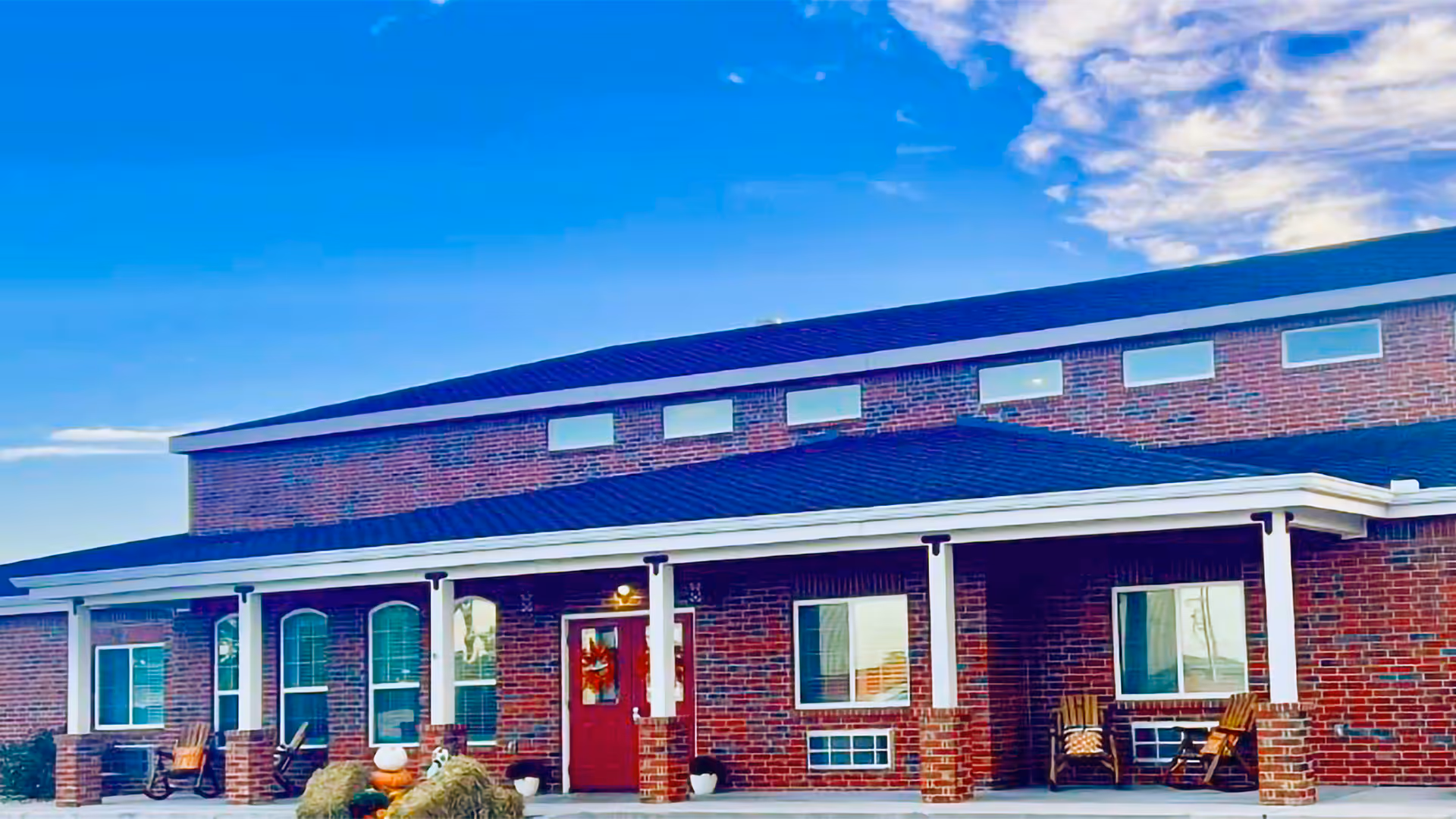 Front exterior of a brick senior living facility with white pillars and covered porch seating.