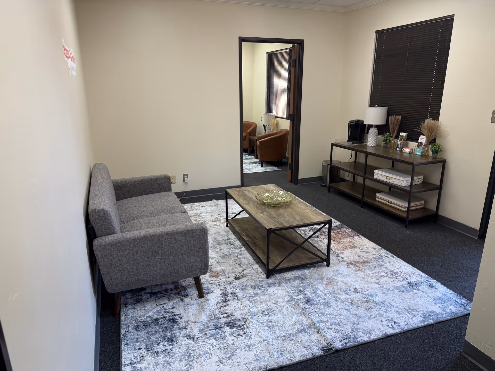 Cozy lounge in a senior facility featuring a grey sofa, coffee table, rug, and shelves.