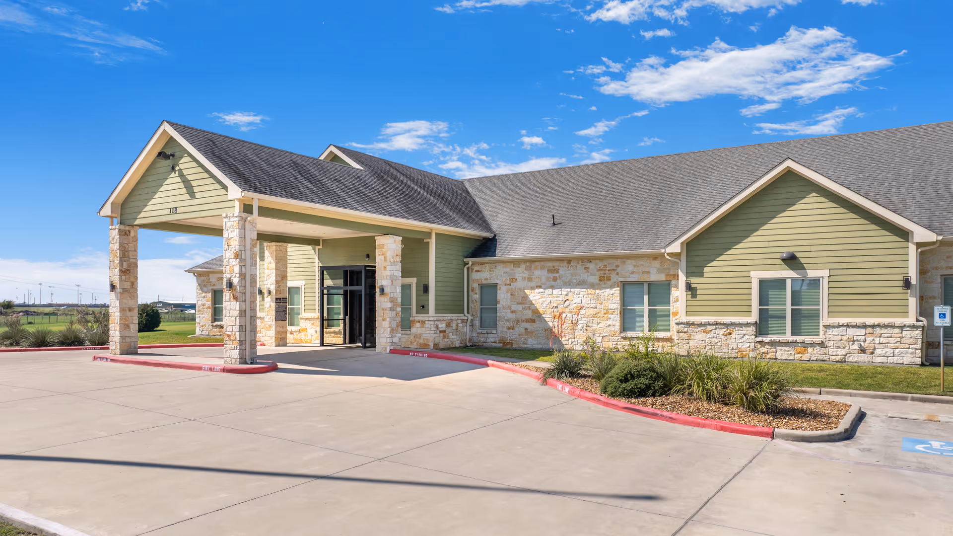 Single-story nursing facility exterior with stone accents, green siding, and a covered front entrance.