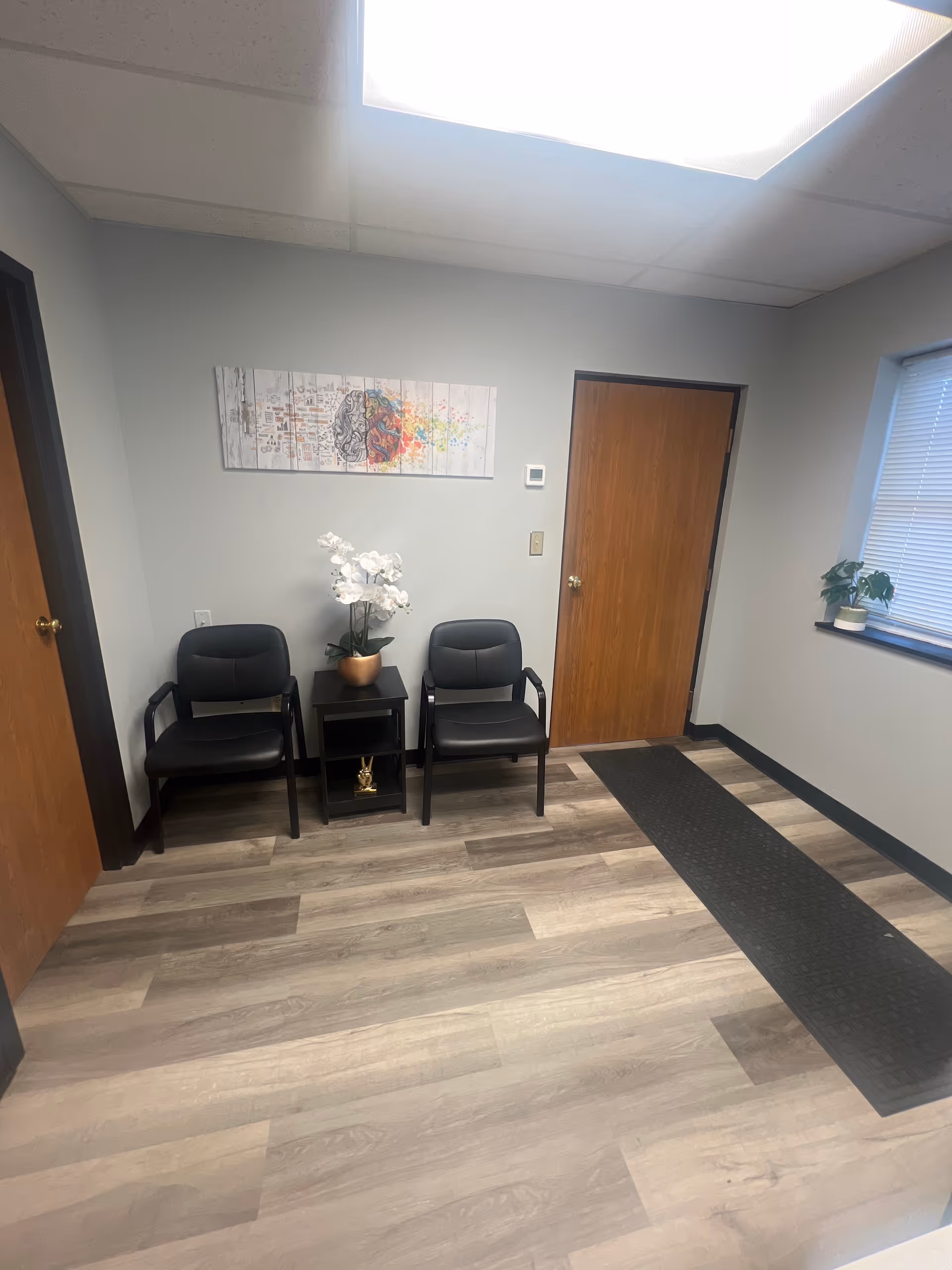 Small waiting area with two black chairs, a side table, white orchid, and wall art.