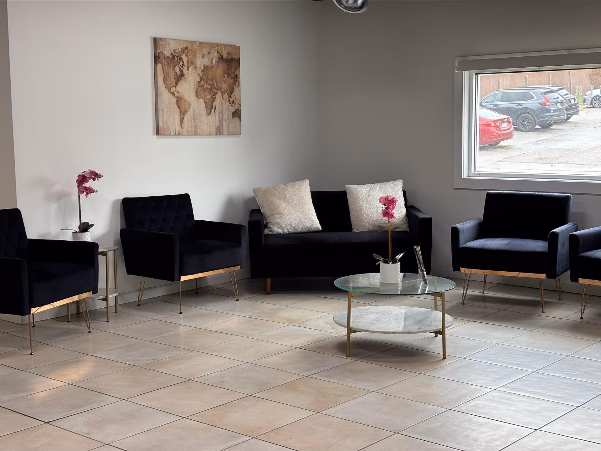 A modern waiting lounge with black chairs, a pink orchid, glass coffee table, and a window.