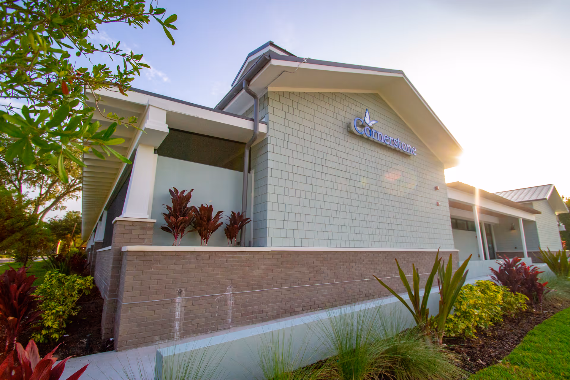 Exterior view of Cornerstone Hospice building with landscaped plants and bright sky.