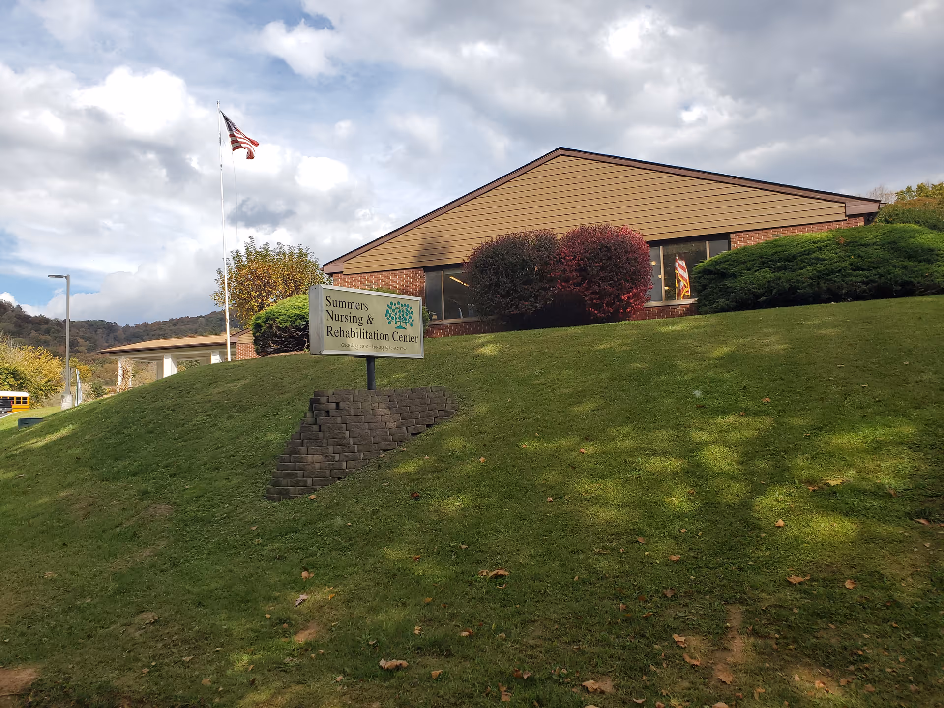 Exterior view of Summers Nursing and Rehabilitation Center on a grassy hillside with a sign.