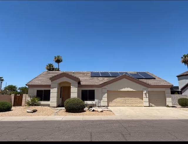 Single-story beige house with two-car garage, desert landscaping, and solar panels on the roof.