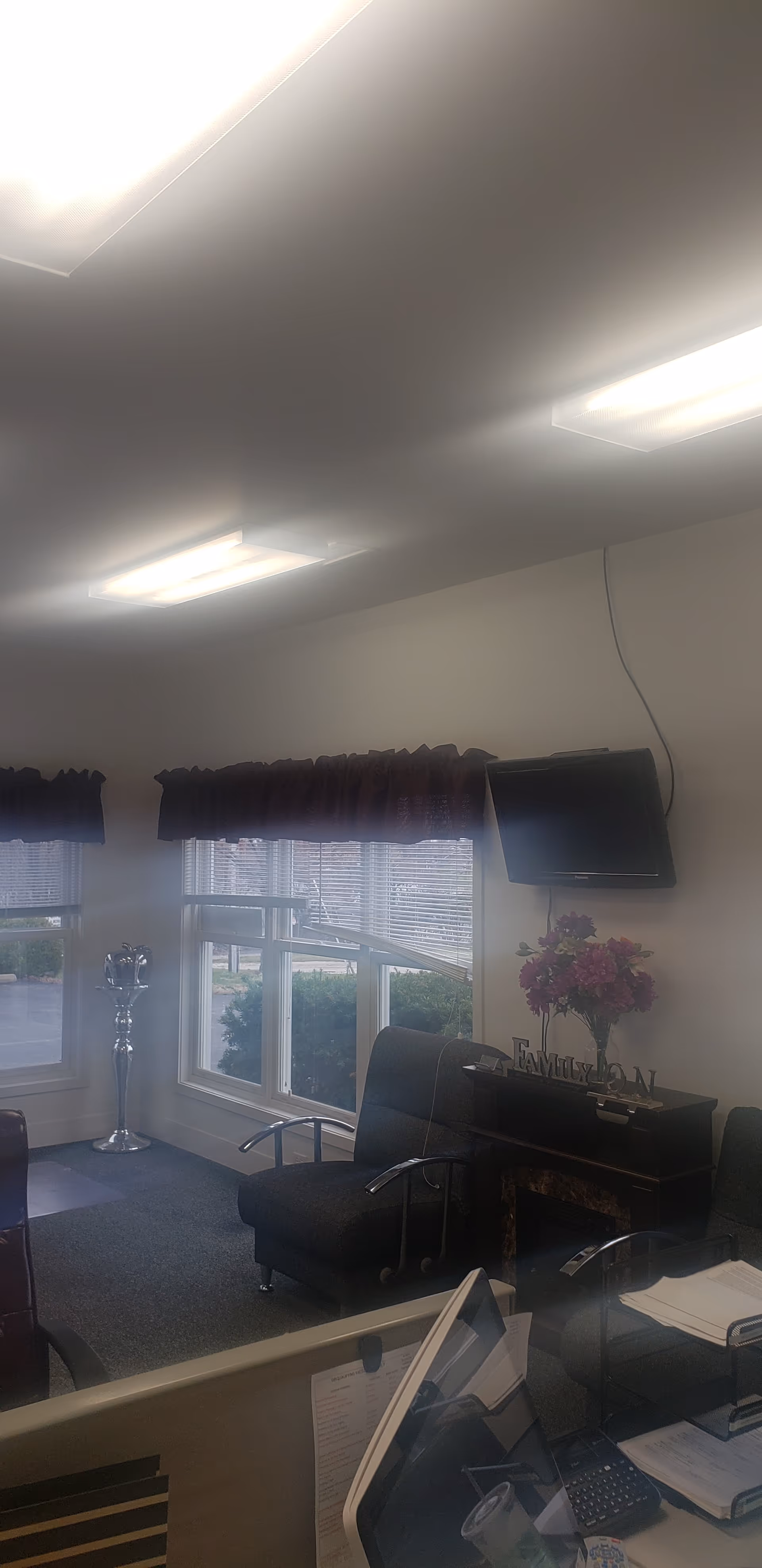 Interior lounge with seating, TV, floral arrangement, and a reception desk by windows.
