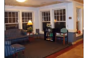 Cozy lounge in a senior living facility with blue sofas, chairs, a lamp, and windows.