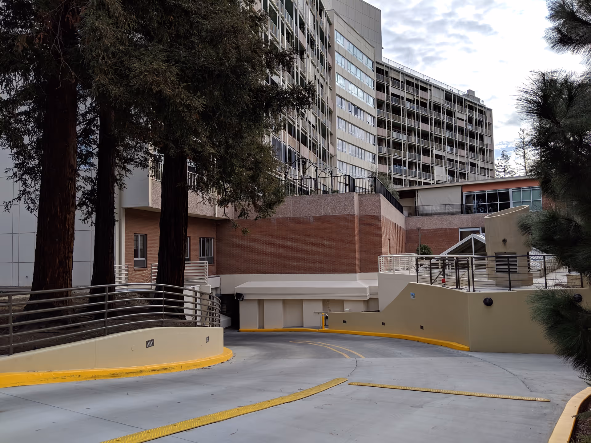Exterior view of a multi-story senior living facility with driveway, ramps, and trees.