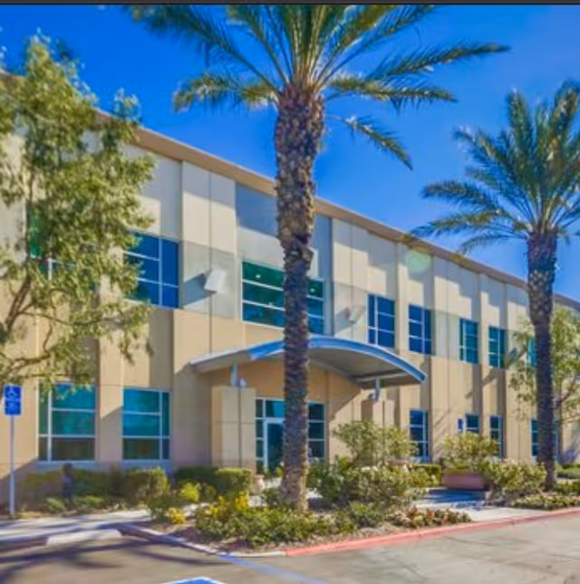 Exterior view of a modern senior living facility with palm trees and a covered entrance.
